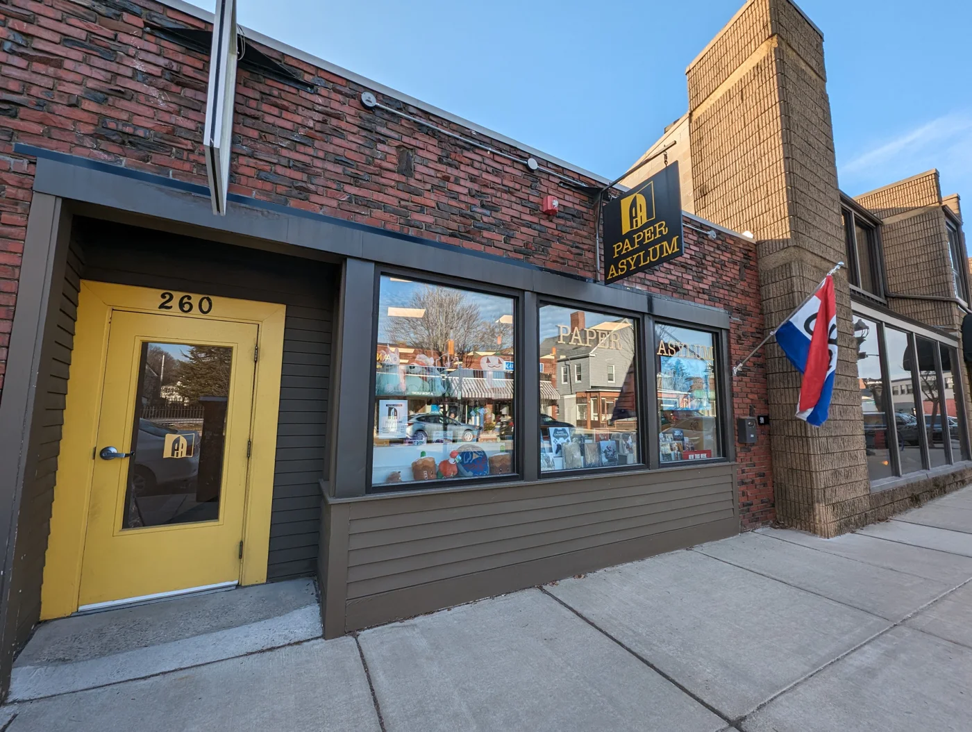 Paper Asylum’s brick storefront and yellow door at 260 Cabot Street in Beverly